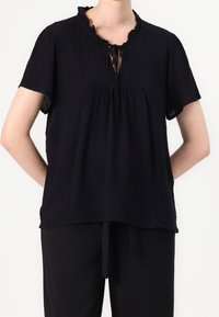 Blusa nera a maniche corte con colletto arricciato, tessuto testurizzato, parte anteriore arricciata e dettaglio del fiocco al collo. Vestibilità ampia con spacchi laterali.