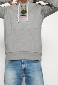 Sudadera gris hecha de tela suave, que presenta un gráfico de un perro de dibujos animados en la parte frontal, cordones ajustables y un bolsillo tipo canguro.