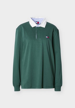 Žalia ilgomis rankovėmis regbio marškinėliai su baltais apykakle ir mažu Tommy Jeans logotipo pleistru kairėje krūtinės pusėje.