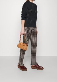 Svart stickad tröja med en texturerad design, bruna och beige rutiga byxor, bruna träskor och en beige handväska med kedjehandtag.
