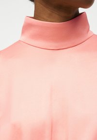 Nærbillede af en person iført et blødt lyserødt højhalset plagg, der viser nakke og øvre brystområde med glat stoftekstur.