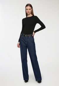Czarna bluzka z długim rękawem w połączeniu z jasnoniebieskimi dżinsami o wysokim stanie i szerokimi nogawkami oraz czarnym paskiem z metalowymi otworami.
