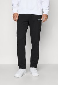 Schwarze Jogginghosen aus Baumwollmischgewebe mit schmalem Schnitt, gesticktem Logo auf dem Oberschenkel und elastischem Bund. Kombiniert mit weißen Sneakers.