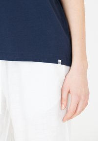 Marinblå bomulls t-shirt med korta ärmar, med en liten vit logotag vid fållen, kombinerad med vita linnebyxor.