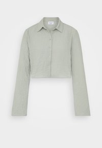 Camisa de manga larga recortada en tejido texturizado de color verde claro. Tiene un cuello clásico y cierre de botones en la parte delantera.