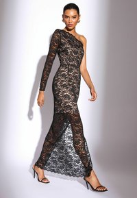 Fekete csipkebársony ruha, amely egy vállon hordható dizájnnal rendelkezik, testhez simuló felső résszel és magas hasítékkal. Átlátszó csipke textúra borítja a bőrszínű bélést, fekete magassarkú cipővel párosítva.