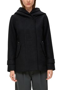 Manteau en laine noire avec capuche, présentant un motif texturé, des poches latérales zippées et de larges poignets, offrant une silhouette structurée.