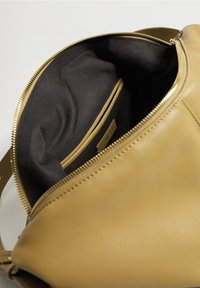 Sac en cuir jaune moutarde ouvert montrant une doublure intérieure en tissu noir et une poche intérieure avec une petite étiquette de marque.