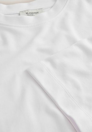 Balta medvilninė marškinėliai su apvalia iškirpte ir trumpomis rankovėmis. Turi lygią tekstūrą ir tvarkingus siūlius palei kraštus.