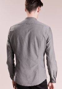 Šedá košile s dlouhým rukávem, která má límec, texturovanou látku a jemné detaily šití. Slim fit s zakřiveným lemem a knoflíkovými manžetami.