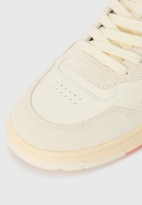 Cream suede and leather sneaker with a textured finish, featuring a perforated toe cap and beige laces, accentuated by a light sole.