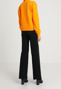 Pomarańczowa bluza z okrągłym dekoltem i ściągaczami na rękawach, zestawiona z czarnymi spodniami o szerokich nogawkach i wysokim stanie oraz czarnymi botkami na platformie.