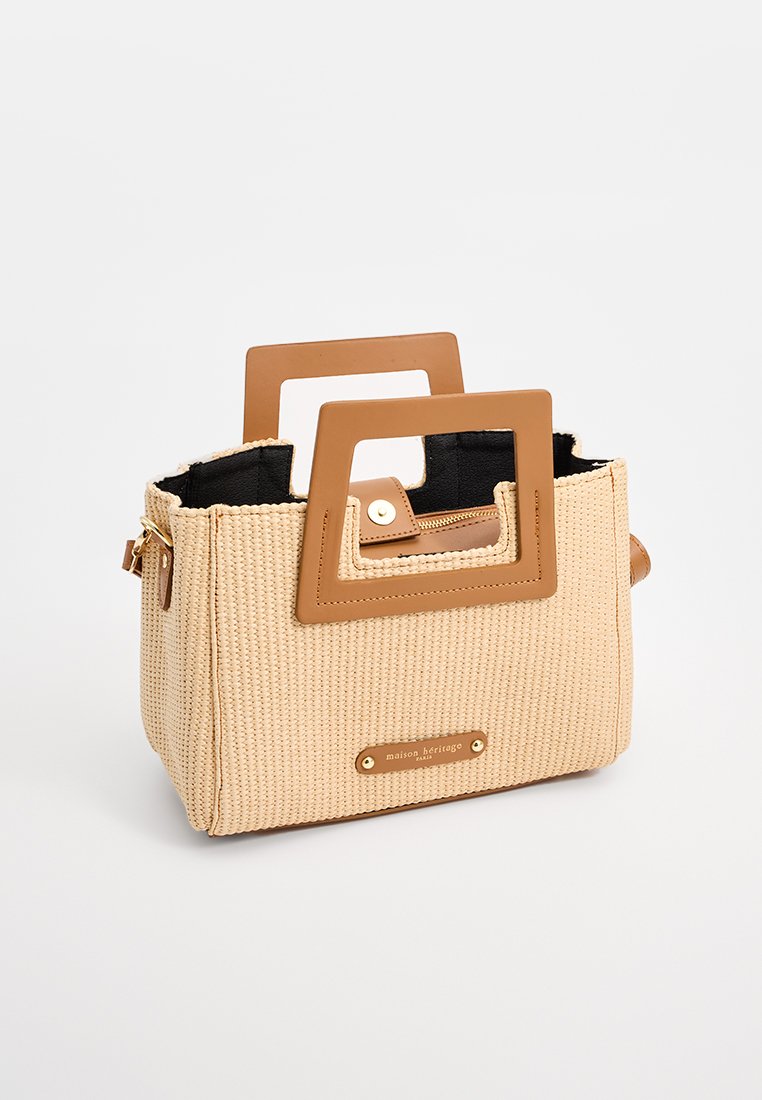 Beige geweven handtas met bruine rechthoekige handvatten en zwarte binnenkant. Heeft messing hardware en een merkplaatje aan de voorkant.