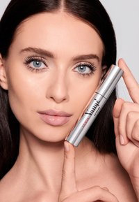 Tubetto di mascara argentato con etichetta "Pupa Vamp! Extreme" tenuto da una persona con pelle liscia e trucco naturale, che mostra occhi azzurri intensi.