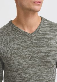 Pullover lavorato a maglia verde khaki con scollo a V, caratterizzato da un motivo testurizzato di fibre chiare e scure. Finitura del tessuto liscia.