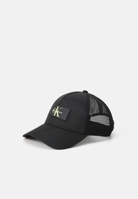 Sort kasket med mesh bagpå, med et rektangulært logo patch i sort og gul. Buet skygge og struktureret design for et tætsiddende look.
