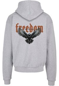 Šedá mikina s kapucí s černou grafikou orla a slovem "svoboda" hnědým písmem nahoře a "kde se setkává strach" dole.