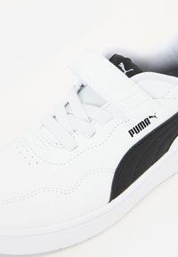 Bijele tenisice s crnim PUMA logotipom, s glatkim sintetičkim gornjim dijelom, detaljima vezivanja i čičak trakama za sigurnu prilagodbu.
