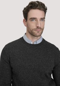 Grau gestrickter Pullover mit rundem Halsausschnitt. Darunter befindet sich ein kontrastierendes hellblaues Hemd mit Kragen, der gesamte Stoff ist strukturiert.