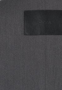 Szara tkanina o teksturowanym splocie; zawiera czarną skórzaną naszywkę z wytłoczonym logo "OPRA", obszywane krawędzie.