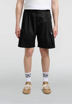 Pantaloncini cargo neri dal taglio ampio, con due tasche laterali e una vita con coulisse. Indossati con calzini bianchi e sneakers beige.