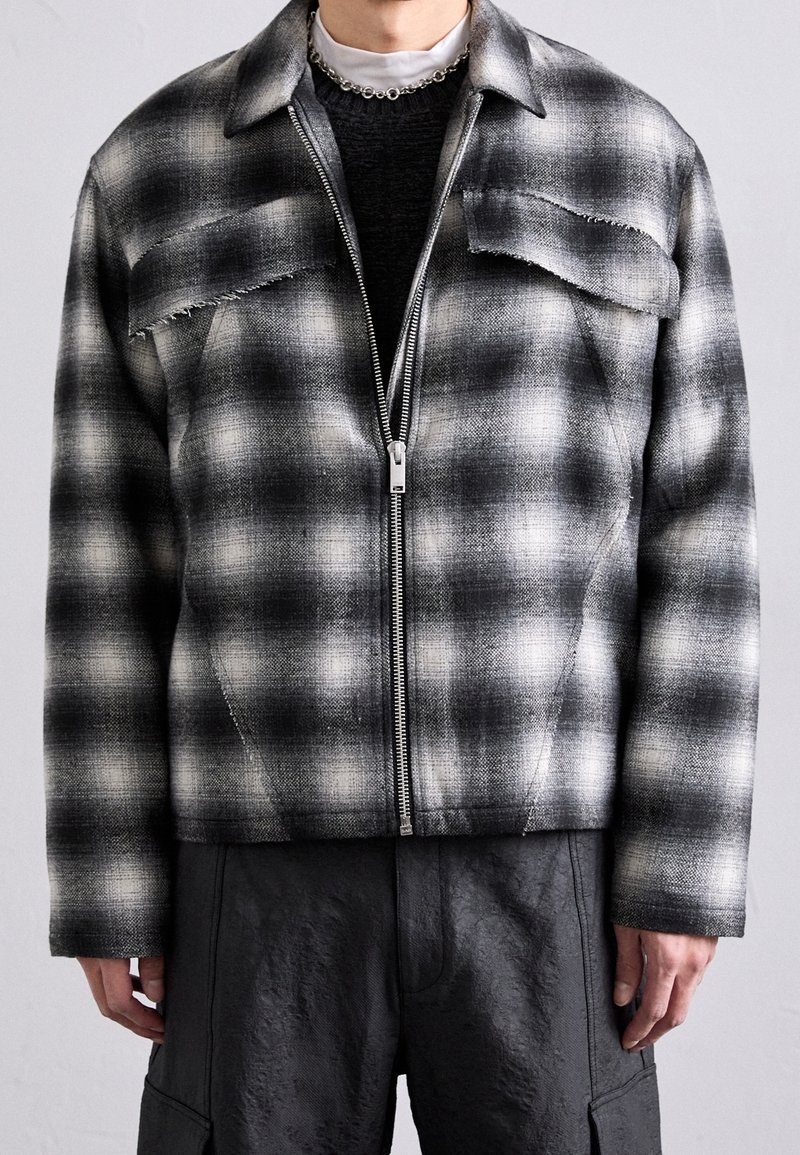 Schwarz-weiße karierte Jacke aus strukturiertem Stoff, mit einem Frontreißverschluss, cropped Design und zwei Brusttaschen mit ausgefransten Kanten.