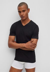 Black short-sleeve V-neck t-shirt made of cotton. Features a subtle logo on the chest, paired with white fitted underwear. Smooth texture.
