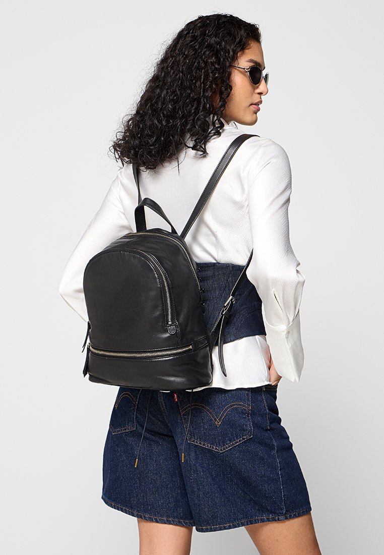 Schwarzer Leder-Rucksack mit runder Form, vorderer Reißverschlusstasche und verstellbaren Trägern, getragen auf dem Rücken einer Person in lässiger Kleidung.