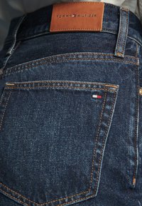 Σκούρο μπλε τζιν από denim με πορτοκαλί ραφές, μια μικρή σημαία Tommy Hilfiger στην πίσω τσέπη και ένα καφέ δερμάτινο λογότυπο στη μέση.