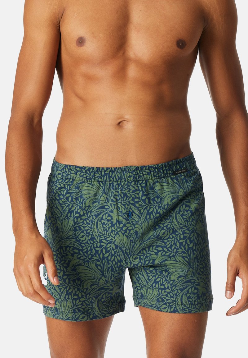 Boxer in cotone blu con motivo a foglie verdi, dotati di una cintura elastica e un singolo bottone nella parte anteriore.