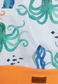 Tessuto in cotone con uno sfondo bianco e motivi colorati di polipi e pesci. Include un pannello inferiore arancione e un'etichetta in pelle.