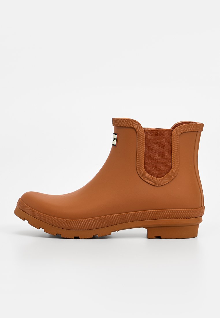 Bottine en caoutchouc marron avec des panneaux latéraux élastiques, semelle texturée, surface lisse et étiquette de marque sur le devant.