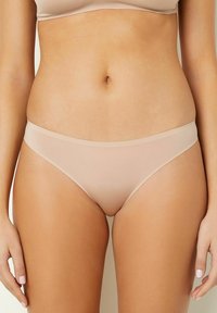 Slip bikini beige senza cuciture con vita bassa e texture liscia, caratterizzato da un design minimalista e senza cuciture visibili o motivi.