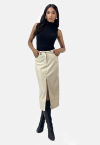 Falda de color crema, de cintura alta, con una abertura frontal, combinada con una camiseta sin mangas negra. La modelo lleva botas altas negras hasta la rodilla.