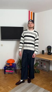 Pull blanc duveteux à rayures noires, pantalon en denim foncé à jambes larges, et mocassins marron avec des chaussettes blanches. Le chapeau présente un détail logo.