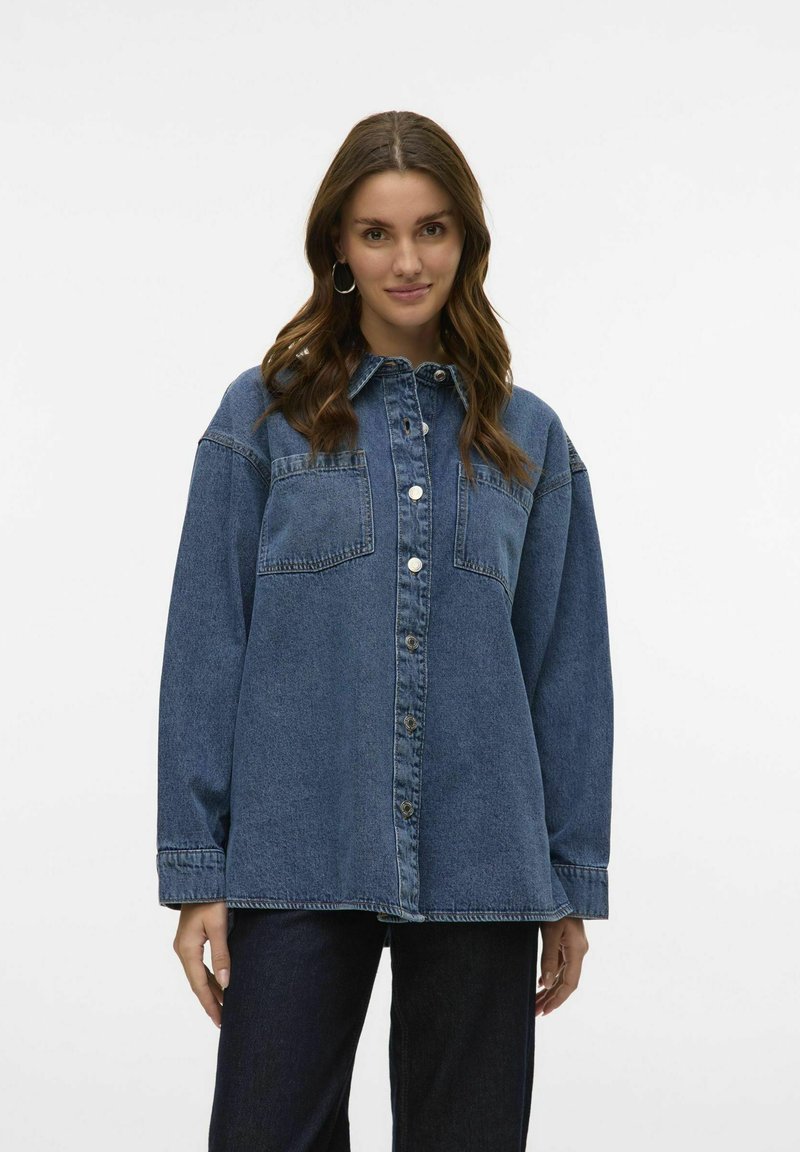Denim shirt in dark blue with a collar, front button closure, two chest pockets, and long sleeves. Distressed accents on the shoulders.
