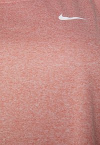 Camiseta deportiva Nike en un color coral claro texturizado con el logotipo de swoosh blanco en la parte superior izquierda. Fabricada con una tela suave y transpirable.