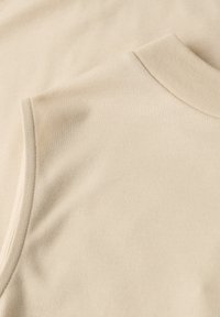 Gros plan sur un tissu beige montrant l'encolure et la couture d'un haut sans manches avec un col côtelé.