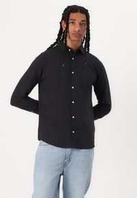 Svart langermet skjorte med knappestolpe, laget av et glatt stoff. Har klassisk krage og en slim fit-design.