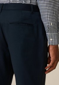 Navyblaue Hosen haben eine glatte Textur und eine Gesäßtasche. Das Modell trägt ein kariertes Hemd mit weißen Knöpfen.