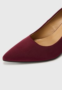 Chaussure plate pour femmes à bout pointu en tissu bordeaux avec doublure intérieure beige et semelle noire, vue en gros plan.