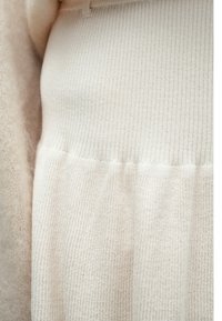 Material bej tricotat cu model de nervuri verticale, având o zonă inferioară texturată. Material moale, ușor, cu un luciu subtil.
