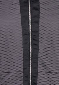 Gros plan sur une fermeture éclair noire sur un tissu gris perforé avec un bord noir, montrant les détails de la texture et des coutures.