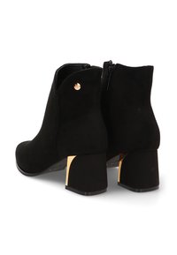 Botines de ante negros con punta redondeada, tacón en bloque con detalles en dorado y cierre de cremallera lateral. Textura suave y diseño minimalista.