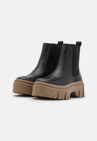 Botas de tobillo de cuero negro con una gruesa suela de plataforma marrón, cuentan con laterales elásticos, tiradores y un acabado liso y brillante.