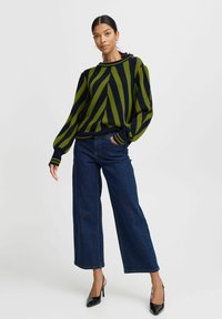 Pull en tricot rayé vert et marine avec des poignets et un ourlet côtelés, accompagné de jeans en denim foncé à jambes larges et de chaussures à talons aiguilles noires.