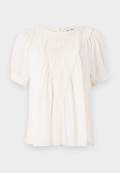 Blusa de crema claro hecha de tela texturizada, con un detalle de volantes en forma de V en el frente, mangas cortas abullonadas y un corte holgado.
