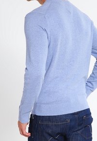 Pull tricoté bleu clair avec un col rond, des poignets et un ourlet côtelés. Le tissu semble doux avec une texture lisse. Porté avec un jean foncé.