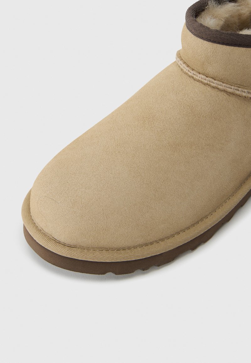 Tan suede boot with a rounded toe, brown fleece lining at the cuff, and a textured rubber sole for grip. Stitched detail along the upper.