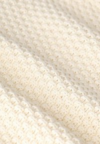 Cream-colored knitted fabric with a textured pattern, featuring intertwined yarns creating a consistent, soft surface.